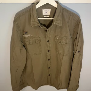 Lexington Overshirt - Klassisk militärinspirerad overshirt från Lexinton i färgen Khaki. Lite mindre i storleken. Skicket är mycket bra!