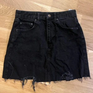 Svart jeanskjol - Svart jeanskjol med kort passform och slitna detaljer som ger en cool vibe. Använd vid få tillfällen. Kjolen är i storlek L/40 men är snarare M/38.