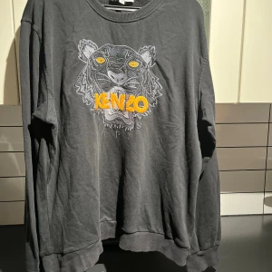 Svart Kenzo sweatshirt med tigerbrodyr - Svart sweatshirt från Kenzo med ikonisk tigerbrodyr och gult Kenzo-tryck framtill. Tröjan har rund hals, långa ärmar och är tillverkad i mjuk bomull. Perfekt statement piece för dig som vill sticka ut.