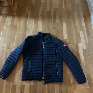 Mörkblå Colmar pufferjacka - Snygg mörkblå pufferjacka från Colmar med quiltad design och två dragkedjeförsedda fickor. Jackan har hög krage, lång ärm och klassisk logga på ärmen. Perfekt för kyliga dagar och enkel att matcha med olika outfits.