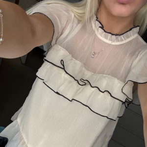 Vit volangtopp - Supersöt topp från Nelly i tunnt material och svarta sömmar. Har använt den en gång så den är i superskick 🤍