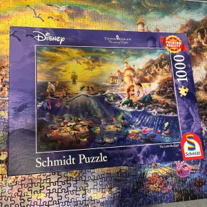 Schmidt Puzzle Disney The Little Mermaid 1000 bitar - Vackert 1000-bitars pussel med motiv från Disney's The Little Mermaid, illustrerat av Thomas Kinkade. Premiumkvalitet, färgstarkt och detaljerat motiv. Perfekt skick, komplett med alla bitar. Passar både samlare och pusselentusiaster.