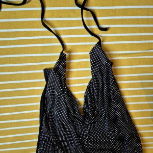 Svart topp - Snygg svart topp med strass stenar  och knytband i nacken. Toppen har en klassisk trekantsform och är perfekt för strandhäng eller party. Materialet känns mjukt och följsamt mot huden. 