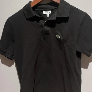 Lacoste piké svart - Säljer nu min Lacoste piké, som tyvärr blivit för liten, använd ganska sparsamt, i ett mycket bra skick. I storlek 164 (14 år), storlek XS ungefär, inga skavanker eller slitningar! Priset är ej hugget i sten!
