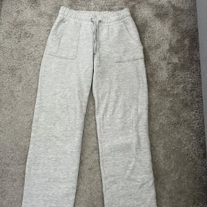 Ljusgrå mjukisbyxor från 157, stl S - Ljusgrå mjukisbyxor från 157 med bred resår i midjan och snörning. Byxorna har raka ben, två stora fickor framtill och är gjorda i mjukt bomullsmaterial. Perfekta för chill dagar eller när du vill vara extra bekväm.