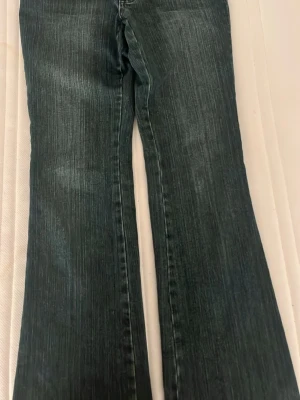 Bootcut jeans med bruna detaljer - Snygga mörkblå bootcut jeans med unika bruna detaljer på bakfickan och linningen. Jeansen har klassisk femficksdesign och är tillverkade i slitstarkt denim-material. Passformen är loose och de har en cool tvättad look som ger extra edge.