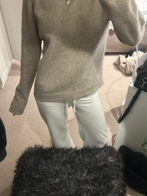 Beige stickad tröja med rund hals - Mysig beige stickad tröja med rundad hals och ribbade muddar vid ärmslut och nederkant. Tröjan har en loose passform och långa ärmar, perfekt för att chilla eller hänga med kompisar. Enkel och stilren design som funkar till många olika outfits.