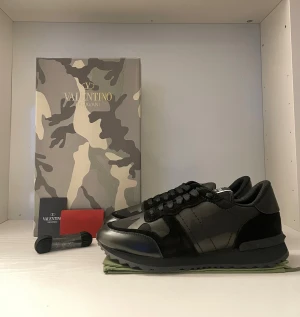 Valentino Garavani Rockrunner  - Säljer ett par svarta Valentino Garavani Rockrunner sneakers i storlek 43. Skorna har coola camouflagemönstrade paneler i skinn och mocka, samt svarta snören och platt sula. Kommer med originalkartong och extra skosnören. Perfekta för dig som gillar exklusiva detaljer. Utan box