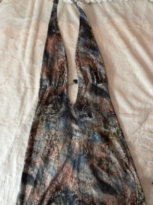 Långklänning  - Lånklänning från Shein med mönster i blått, brunt och grått. Klänningen har halterneck med knyt i nacken, djup v-ringning och ett hjärtformat smycke framtill. Oanvänd