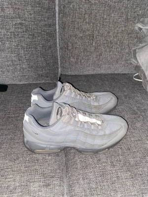 Nike Air Max 95 grå sneakers - Säljer ett par grå Nike Air Max 95 sneakers med snygga vågiga paneler och synlig Air-dämpning i sulan. Skorna har snörning och är tillverkade i mesh och syntetmaterial för en cool och sportig look. Perfekta för dig som gillar streetwear och vill ha något som sticker ut.