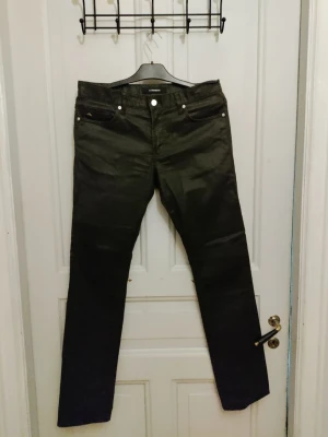 Svarta straight jeans från J.Lindeberg - Snygga svarta jeans från J.Lindeberg med klassisk femficksdesign och silverfärgade detaljer vid knappar och nitar. Byxorna har rak passform och är tillverkade i ett slitstarkt bomullsmaterial med en lätt glansig finish. Perfekta för dig som gillar stilrena och tidlösa plagg.