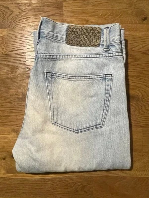 Ljusblå raka ”our legacy” jeans med flätad patch  - Säljer ett par ljusblå jeans med rak passform och klassisk femficksdesign. Jeansen har en unik flätad patch vid linningen bak som ger en cool detalj. Materialet är jeans och färgen är ljusblå med lite tvättad look. Perfekt för dig som gillar avslappnad stil.