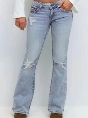 Bootcut ljusblå jeans med slitningar - Bootcut jeans i ljusblå tvätt med slitna detaljer på lår och knän. Klassisk femficksmodell med knapp och dragkedja framtill. Materialet är jeans och passformen är loose med något utsvängda ben. Snygga fickdetaljer bak. Passar mig som har storlek 34 i jeans.