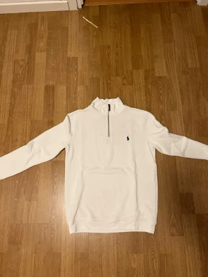 Vit half zip tröja från Polo Ralph Lauren - Säljer en stilren vit långärmad tröja från Polo Ralph Lauren med half zip och klassisk broderad logga på bröstet. Tröjan har en hög krage och är gjord i mjuk bomull, perfekt för chill dagar. Passformen är normal och den funkar grymt till jeans.