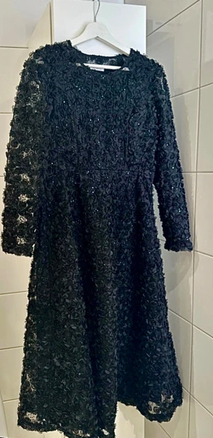  Ida Sjöstedt super snygg klänning med rosor - Passar perfekt till julfest eller julbord/ nyårsafton. Jätte bra skick/Magisk svart klänning från Ida Sjöstedt med 3D-blommor och paljetter över hela klänningen. Klänningen har lång ärm i transparent mesh med blommiga detaljer och rund halsringning. Perfekt för dig som vill sticka ut med en unik och elegant look.