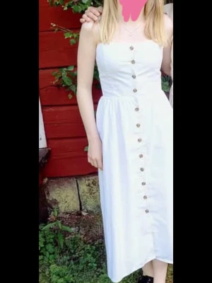 Vit klänning med knappar - Säljer en vit långklänning med smala axelband och bruna knappar längs hela framsidan. Klänningen har en rak passform med smock i ryggen. Använd fåtal gånger. Skriv gärna om du har frågor och läs min bio innan du köper💗💗 Kan diskutera priset🙏🙏