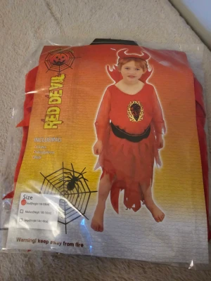 Röd djävulsväst barn, Halloween - Röd väst för barn med eldigt tryck och svarta detaljer, perfekt till djävulskostym. Ingår i set med klänning, bälte och huvudbonad. Tillverkad i lätt polyester och har taggiga kanter för extra effekt.