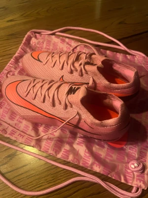 Nike Mercurial Air Zoom rosa fotbollsskor nya elite - Säljer ett par Nike Mercurial Air Zoom fotbollsskor i en snygg rosa färg med orange och svarta detaljer. Skorna har snörning, platt sula med dobbar och en cool grafisk logga på sidan. Ovandelen är i syntetmaterial för lätt känsla och bra grepp på planen.