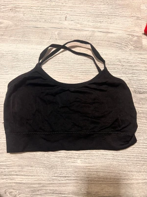 Svart ärmlös sporttopp - Säljer en svart sporttopp med smala axelband som korsas i ryggen. Perfekt för träning eller chill. Materialet känns mjukt och stretchigt.