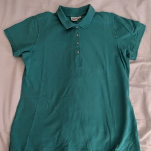 Turkos pikétröja från CRW - Säljer en snygg turkos pikétröja från CRW. Tröjan har korta ärmar och en klassisk krage med knappar framtill. Perfekt för en avslappnad stil.