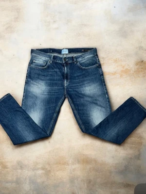 Blå jeans från Dondup, straight fit - Säljer ett par klassiska blå jeans från Dondup, Made in Italy. Jeansen har en rak passform med fem fickor och snygga slitningar på låren. Materialet är robust denim i bomull och de har normal midja. Perfekta för dig som gillar tidlös stil och italiensk design.
