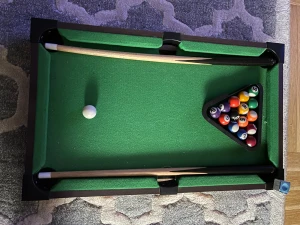 Grön minibiljardbord med tillbehör - Säljer ett minibiljardbord med grön filt, två träköer, set med färgglada biljardbollar och en svart triangel för uppställning. Perfekt för att spela hemma med kompisar. Bordet har svarta kanter och är kompakt i storleken, lätt att flytta runt.