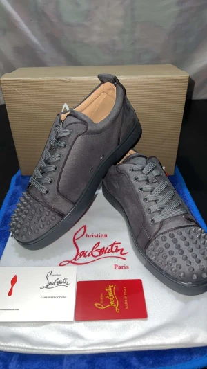 Christian Louboutin gråa sneakers med nitar - Säljer ett par gråa sneakers från Christian Louboutin med coola nitar på tån och klassisk röd sula. Skorna har snörning, rund tå och är tillverkade i mocka med detaljer i skinn. Perfekt för dig som vill sticka ut med en lyxig och edgy stil.