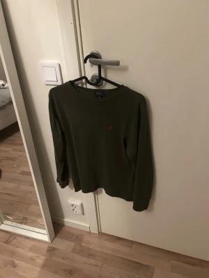 Olivgrön långärmad tröja Polo Ralph Lauren - Säljer en olivgrön långärmad tröja från Polo Ralph Lauren i storlek M. Tröjan har en klassisk rund hals och en liten röd broderad logga på bröstet. Tillverkad i mjuk bomull viktigt att tillägga storlek m i barn motsvarar typ 152