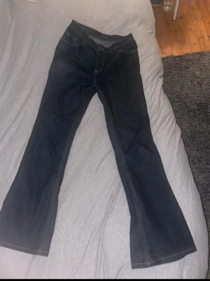 Mörkblå bootcut jeans från Amisu - Säljer ett par mörkblå jeans från Amisu med bootcut-snitt och hög midja. Klassisk femficksmodell med kontrastsömmar och dragkedja. Materialet är jeans med en mjuk känsla och snygg passform som ger en schysst siluett.
