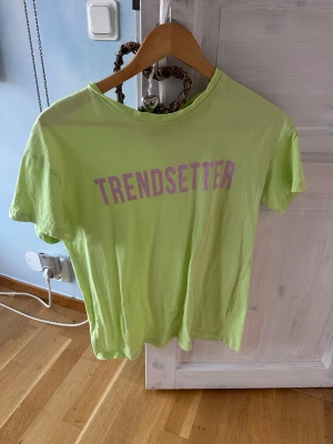 Ljusgrön t-shirt med tryck från Bershka - Fräsch ljusgrön t-shirt från Bershka i storlek XS med lila texten 'TRENDSETTER' på bröstet. Klassisk rund hals och korta ärmar. Perfekt för dig som gillar att sticka ut och vill ha en cool statement-tee i garderoben. Materialet är mjuk bomull.