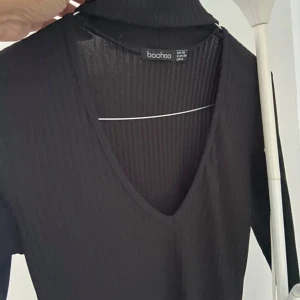 Svart ribbad polotopp från Boohoo - Svart långärmad polotopp från Boohoo i ribbad polyester. Toppen har en djup v-ringning framtill och en hög krage. Materialet är stretchigt och figurnära, perfekt att styla med jeans eller kjol. Enkel och stilren design som funkar året runt.använd 1 gång. Mycket bra skick hämtas i Norsborg Botkyrka 