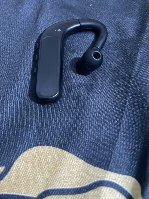 Bluetooth mono headset - Trådlös Bluetooth mono-headset med öronkrok, perfekt för handsfree-samtal. Svart färg, synligt i gott skick med mindre slitage på ytan. Bekväm passform och enkel kontroll via knappar på sidan. Passar både arbete och bilkörning.