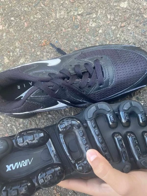 Svarta Nike Air Max sneakers - Säljer ett par svarta Nike Air Max sneakers med cool transparent sula och klassisk snörning. Ovandelen är i mesh och syntet med vita detaljer på sidan. Perfekta för dig som gillar sportig stil och vill ha bekväma skor med unik design.