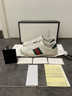 Gucci Ace skor - Säljer dessa feta Gucci Ace skor. En liten defekt vid högra hälen (se bild 6), snörerna är även lite smutsiga annars Bra skick. Storlek 8,5 US motsvarar 42,5 ungefär. Allt og medkommer samt äkthetscertifikat och kvitto. Pris kan självklart diskuteras!!