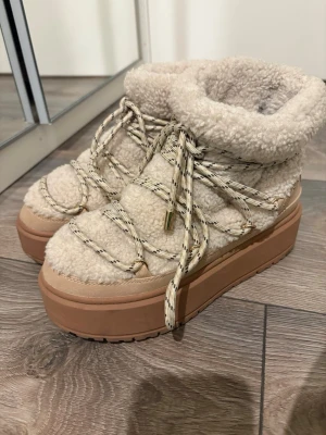 Beige boots - Säljer ett par beige boots med plattformssula från Bershka. Skorna har snörning med grova beige och svarta snören, samt en fluffig yta i syntetpäls och mockadetaljer. Perfekta för kalla dagar och har en rund tå. Har haft på mig dom två gånger. 