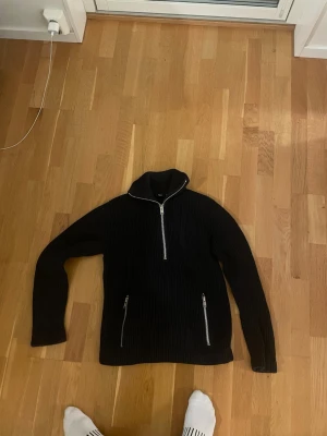 Svart stickad tröja från Filippa K - Svart ribbstickad tröja från Filippa K i storlek M. Tröjan har en hög krage och half zip framtill samt två dragkedjeförsedda fickor. Materialet är mjukt och stickat, perfekt för kyliga dagar. Enkel och stilren design som funkar till många olika looks. Grym kvalitet på tröjan. Mycket vikt i materialet