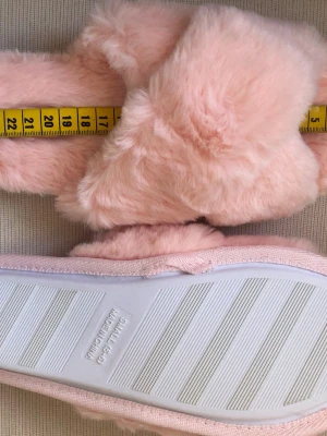 Nya Fluffiga rosa sandaler från Ivora i storlek Small - mått se bilder  - Supersöta fluffiga sandaler från VORA i ljusrosa syntetpäls. De har korslagda band över foten och en mjuk, vadderad innersula. Perfekta för att mysa runt hemma och ger en riktigt cozy vibe.