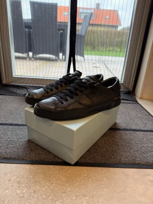  Philippe Model svarta - Säljer ett par svarta Philippe Model sneakers med rund tå och platt sula. Skorna är tillverkade i skinn och har klassisk snörning. Diskret branding på sidan och tungan. Perfekta för dig som gillar stilrena och tidlösa sneakers. Ny pris är runt 5 tusen och har ni fler frågor är det bara att skriva, 100% äkta. Box pch dustbag ingår men skoträ ingår ej