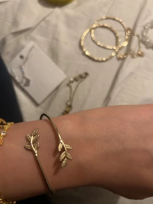 Guldfärgat armband med blad - Snyggt guldfärgat armband i öppen design med detaljerade blad i båda ändarna. Armbandet har en tunn och stilren form som ger en trendig och elegant känsla. Perfekt accessoar för dig som gillar naturinspirerade smycken.