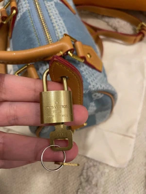 Louis Vuitton denim handväska - Superfin handväska från Louis Vuitton i blått denimtyg med rutigt mönster och ljusbruna skinnhandtag. Väskan har guldfärgade metalldetaljer, dragkedja och medföljande lås med nyckel. Perfekt storlek för det viktigaste och riktigt snygg streetstil.