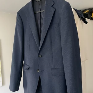 Kostym från Bläck - Snygg mörkblå perforerad kostym från Bläck med modern, skräddad passform. Kavajen har två knappar, klassiska fickor och diskret struktur i tyget. Kavaj strl 50, byxor 54