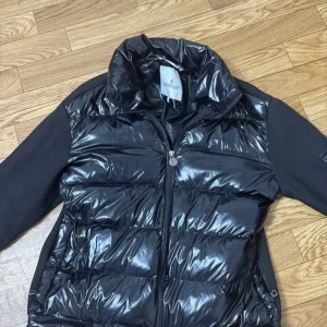 Svart pufferjacka från Moncler - Den är i jätte bra skick har haft i 9 månader och känns som ny hela tiden. Qr koden funkar och den på armen funkar oxå hade dock ingen annan mobil för att visa att den funka. Säljer pga jag fick en ny i födelsedags present och inte behöver denna mer. Jag älskar hur den ser ut medan jag har på mig den och hur skönt det är att ha på sig den ute där den kan användas i kyla och värme. Helst vill jag inte sälja den men vinner inte på att ha två styckna samtidigt. Den har sönder tagna kedja bitar.