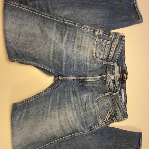 Replay Anbass ljusblå jeans herr - ( Modellen är 173cm lång) Säljer ett par Replay Anbass jeans i ljusblå tvätt med snygga slitningar. Klassisk femficksmodell, normal passform och smalare ben. Jeansen har läderpatch med Replay-logga bak och är tillverkade i mjukt bomullsmaterial med stretch för extra komfort.  Det är bara att slå en pling 🛎️ ❗️ om några funderingar.