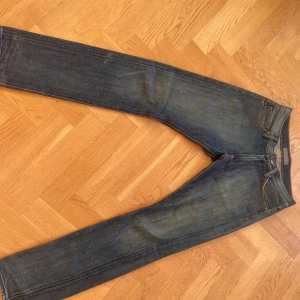 Blå jeans från Acne Jeans - Säljer ett par klassiska blå jeans från Acne Jeans med snygga orangea sömmar och detaljer. Modellen har rak passform och normal midja, tillverkade i slitstarkt denimtyg. Perfekt för dig som gillar stilrena och tidlösa jeans.