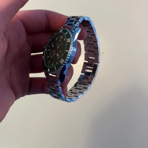 Silverfärgad klocka från Pier One - Stilren klocka från Pier One med rund svart urtavla och silverfärgat armband i metall. Urtavlan har tydliga siffror och flera små visare för extra funktioner. Perfekt accessoar för dig som gillar en klassisk look med modern touch.