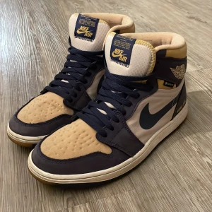 Nike Air Jordan 1 Gore-Tex Highs - Nike Air Jordan 1 Gore-Tex sneakers i high-top modell med beige och mörkblå färgblock. Swoosh-logga på sidan, snörning och rund tå. Yttermaterial i skinn och syntet med Gore-Tex för extra väderskydd. Gula detaljer på plös och krage. Är använda max 2 gånger så helt. Tveka inte och höra av er👍✅