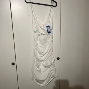 Vit omlottklänning från Shein M - Supersnygg vit långklänning från Shein med smala axelband och draperad omlottfront. Klänningen har rynkade detaljer längs hela längden och en figurnära passform som framhäver siluetten. Perfekt för dig som vill sticka ut med en elegant och trendig look.