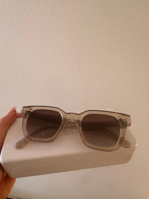 Beige CHIMI solglasögon i fyrkantig form - Snygga solglasögon från CHIMI i modellen ECRU med transparent beige båge och fyrkantig form. Designade i Stockholm och har bruna tonade linser. Riktigt clean look som passar till alla dina sommaroutfits. Kommer med matchande fodral.