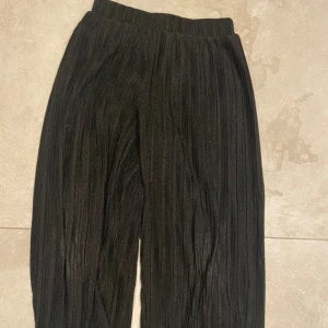 Svarta glittriga byxor Petit Sofie Schnoor - Festliga vida byxor från Petit Sofie Schnoor i storlek 140cm. Byxorna har glittrigt tyg, bred resår i midjan och ett ribbat, plisserat mönster. 