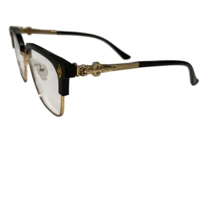 Svart och guldiga glasögon med detaljer - Stilrena glasögon med svart ovandel och guldfärgade detaljer. Rektangulär form med markerad båge och snygga utsmyckningar på skalmarna. Transparenta linser och näskuddar för extra komfort. Perfekt för dig som vill sticka ut med en lyxig vibe.
